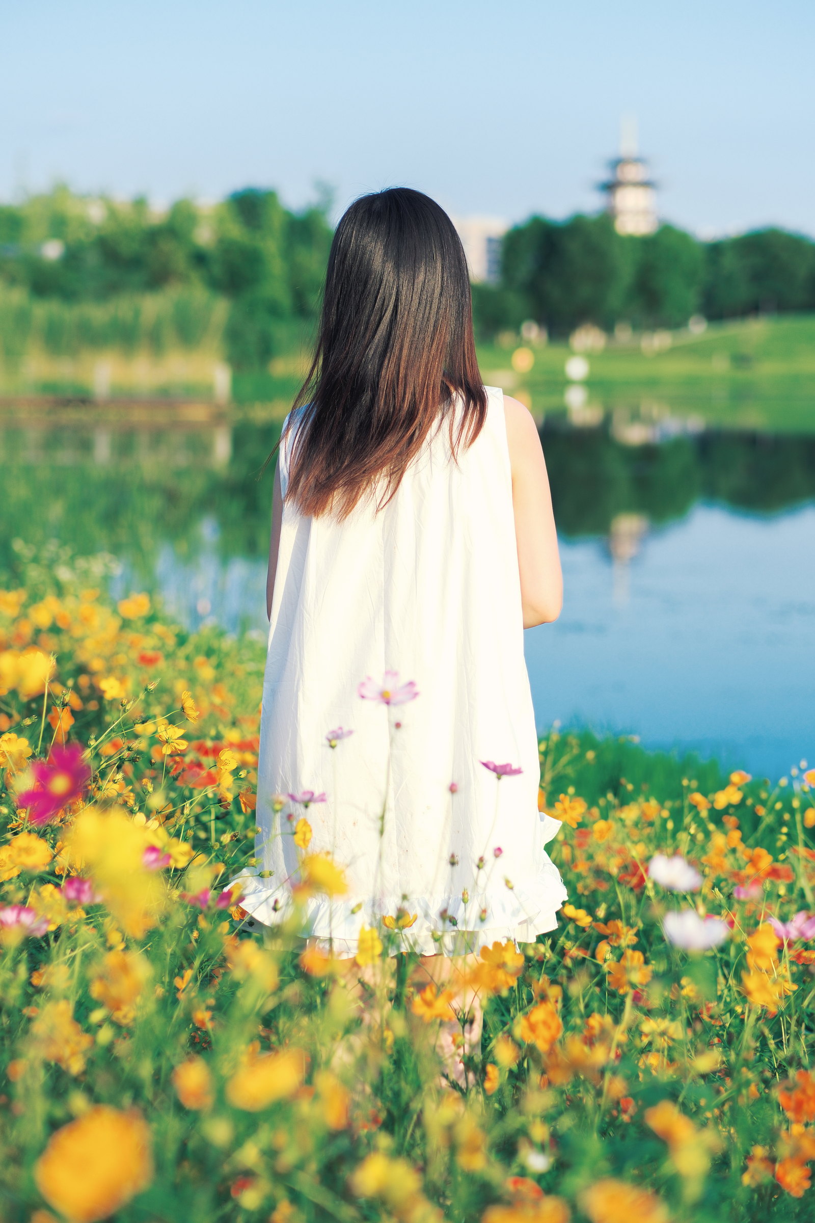 女子白色裙装站在花海与湖水前