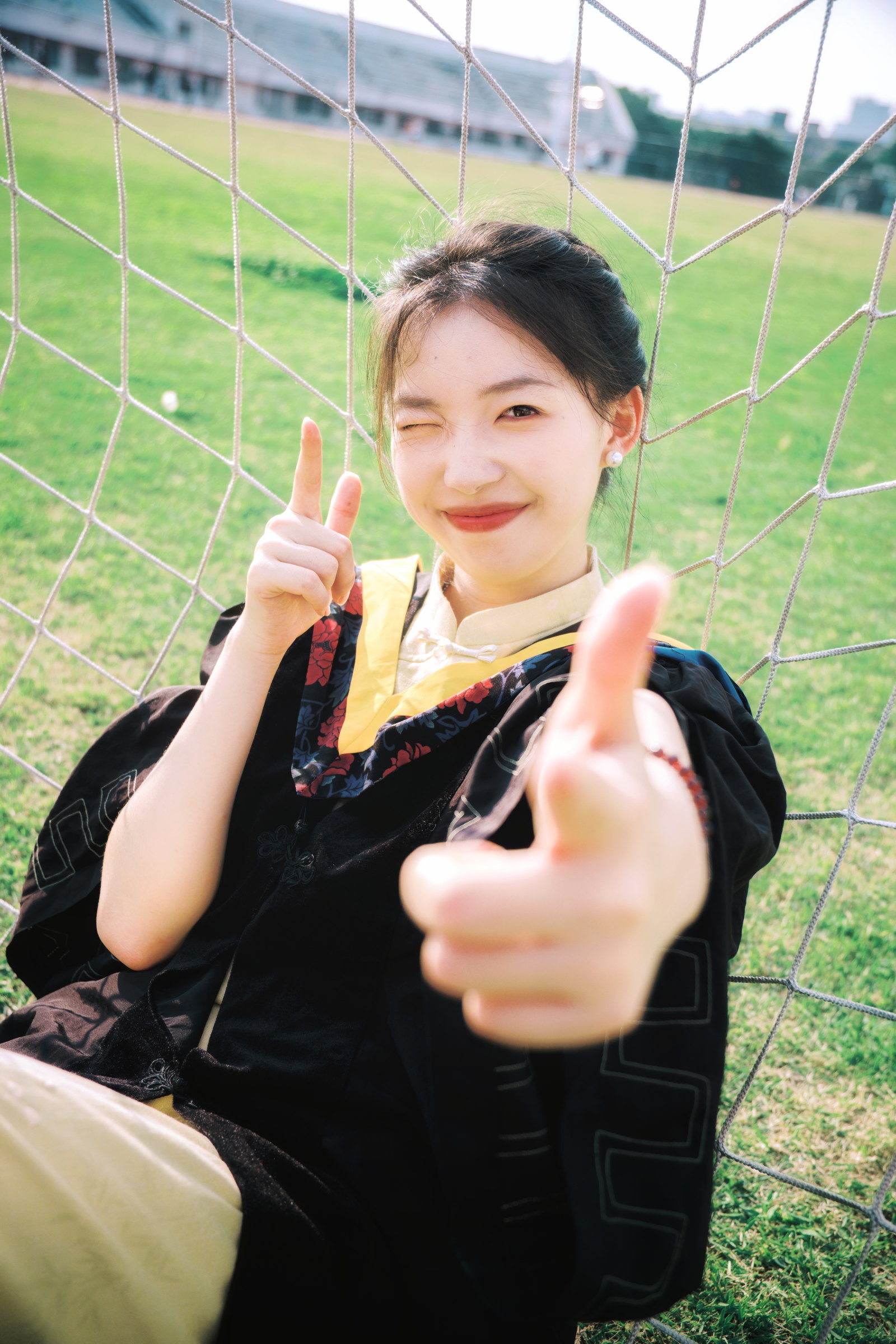 身穿毕业袍的女子坐在草地上的球网旁微笑